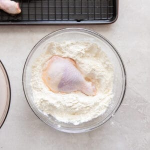 dredging a piece of chicken in flour in a glass bowl