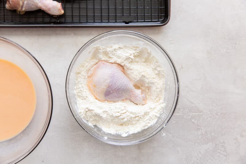 dredging a piece of chicken in flour in a glass bowl