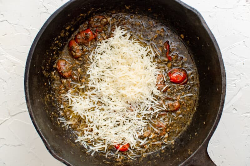 Parmesan cheese added to tomato and pesto sauce in a skillet