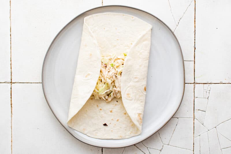 folding tortilla around chicken ranch filling on a white plate