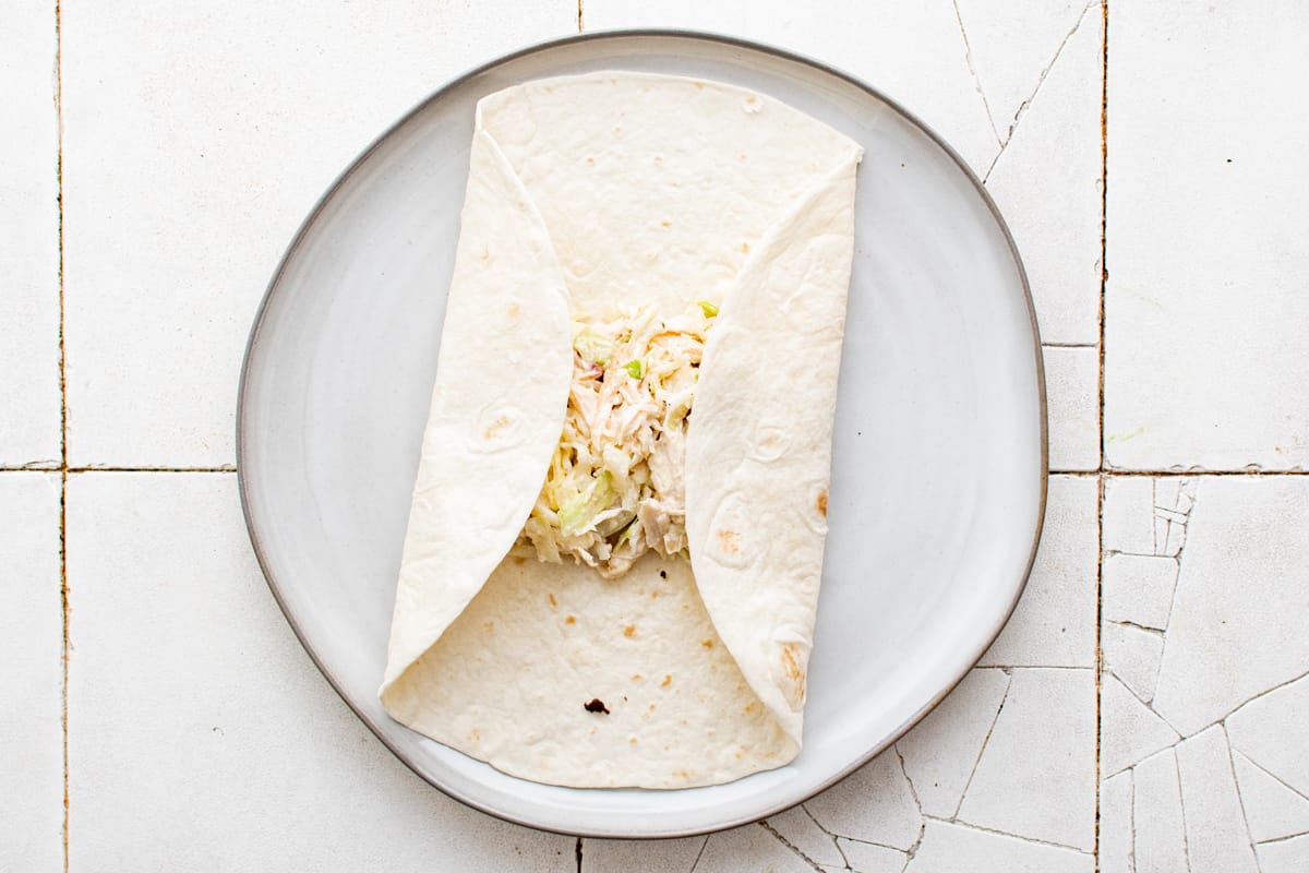 Folding tortilla around chicken ranch filling on a white plate.