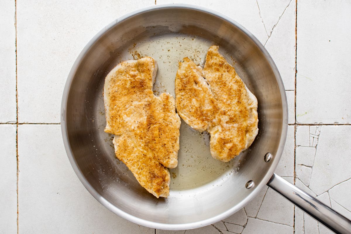 2 chicken breasts cooking in a pan.