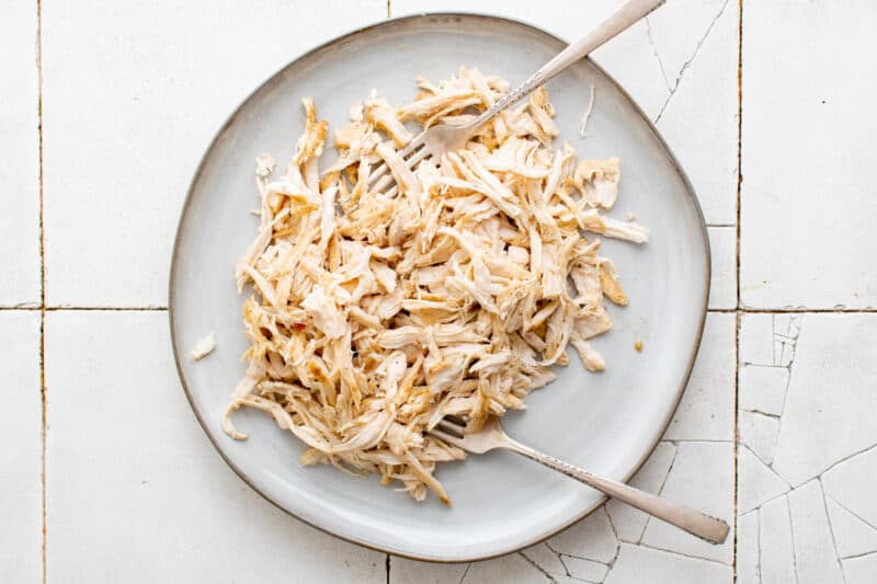shredded chicken breasts on a white plate with 2 forks