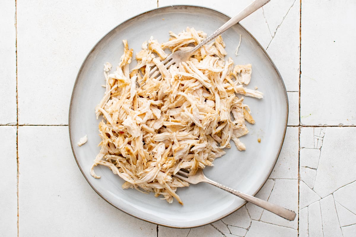 Two forks shredding chicken on a plate.