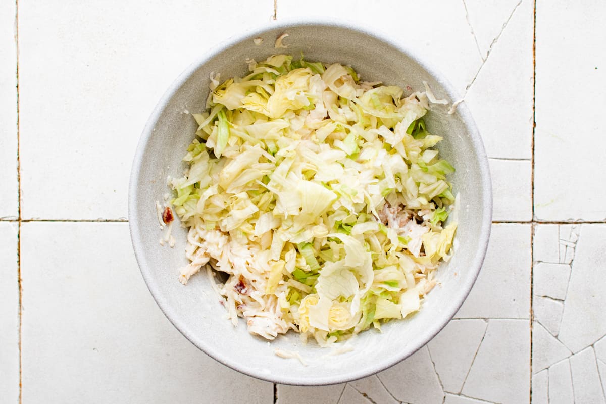 lettuce added to chicken ranch wrap filling in a white bowl.