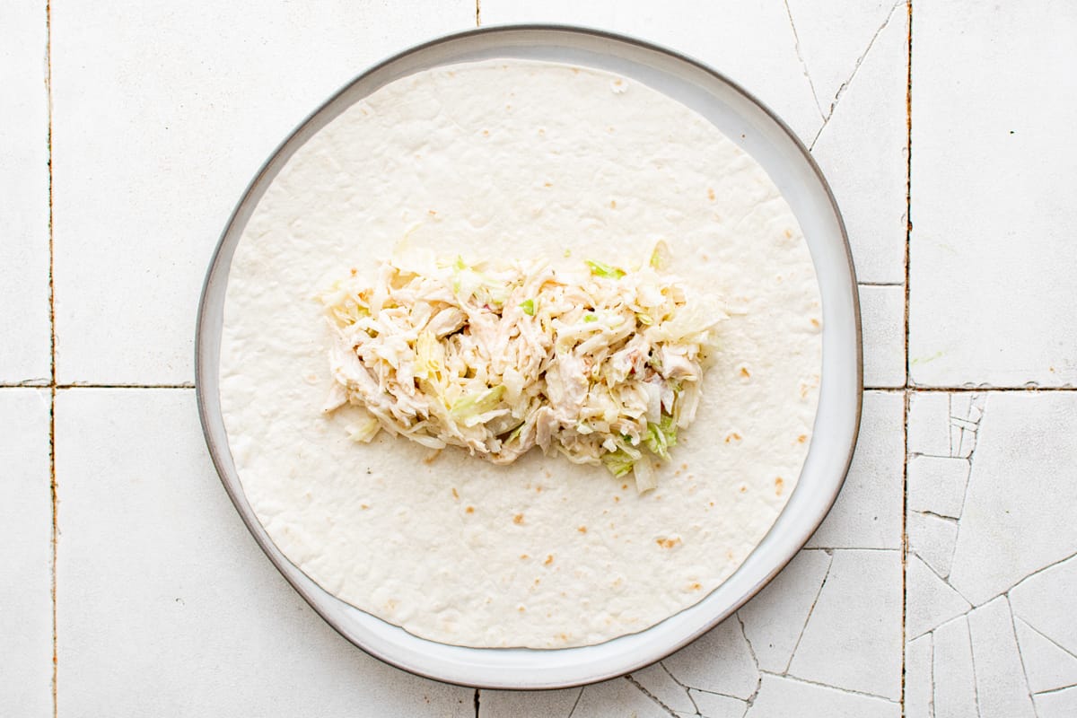 Shredded chicken ranch mixture on a tortilla on a white plate.