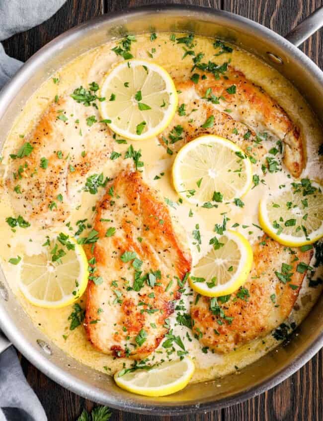 overhead image of lemon parmesan chicken breasts in a skillet with lemon slices and parsley