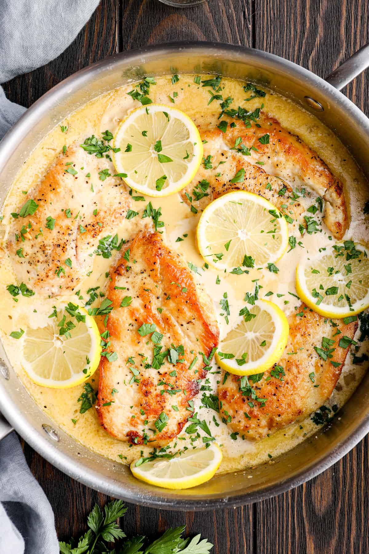 overhead image of lemon parmesan chicken breasts in a skillet with lemon slices and parsley