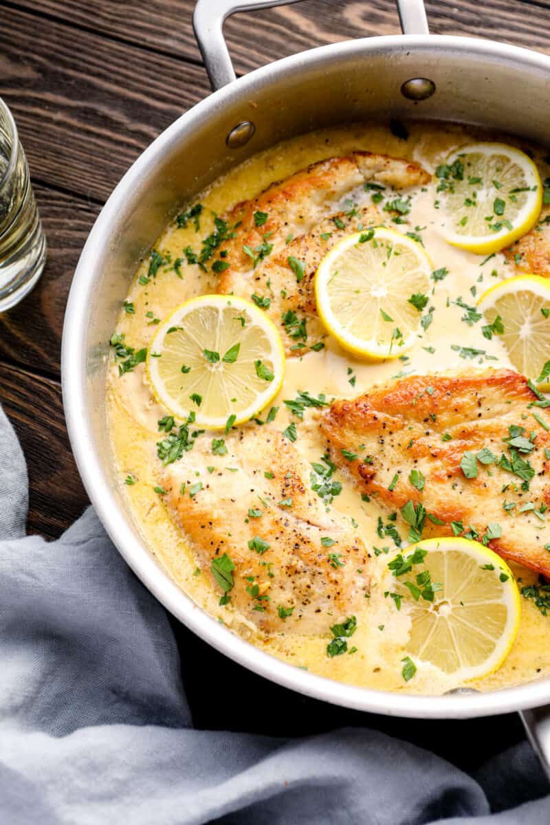 lemon parmesan chicken breasts in a skillet with lemon slices and parsley