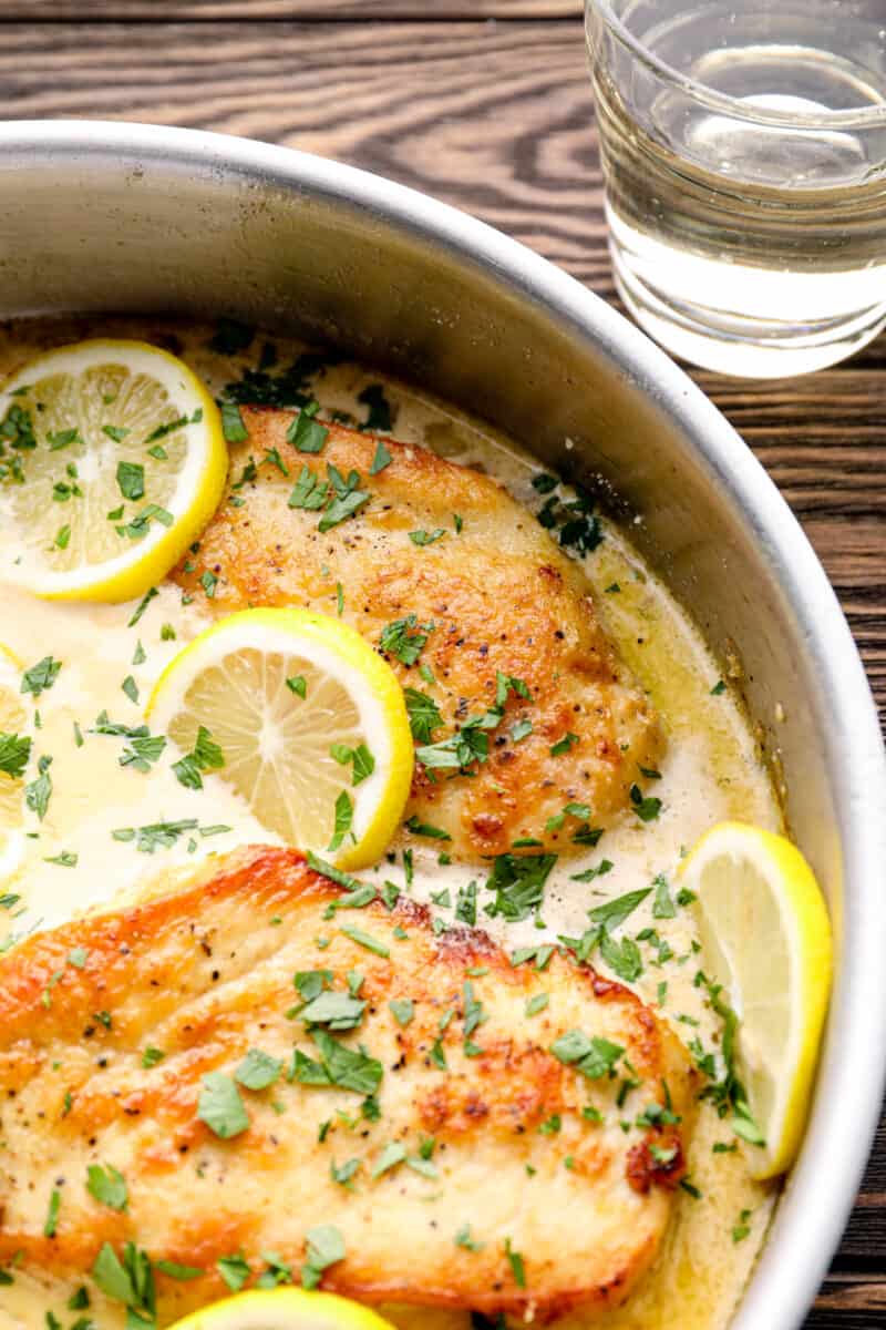 lemon parmesan chicken breasts in a skillet with lemon slices and parsley