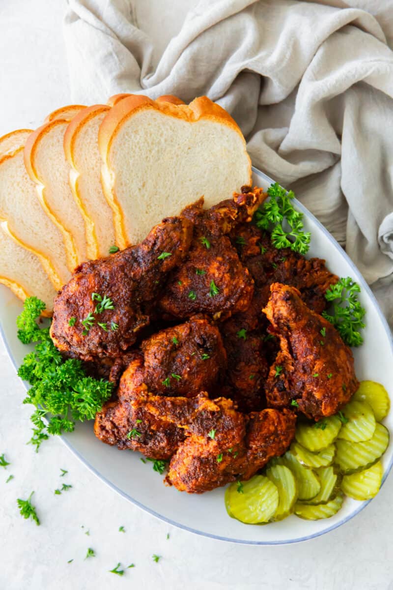 spicy fried chicken on a white platter with slices of white bread and pickles