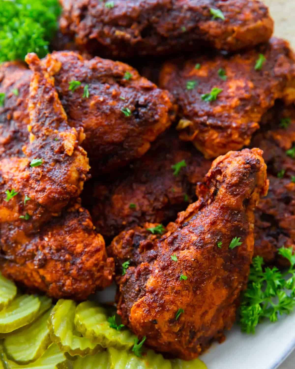 pieces of fried nashville hot chicken n a platter with pickles.
