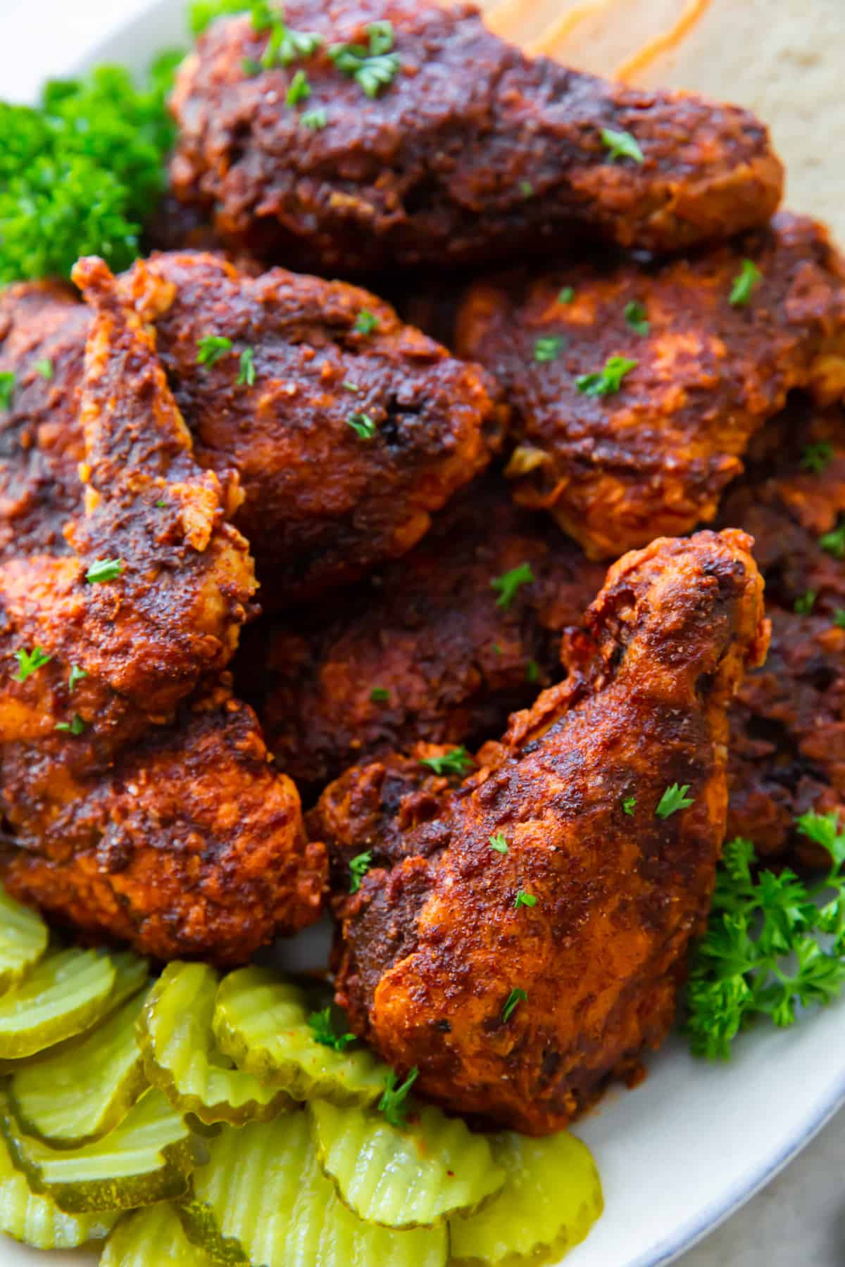 spicy fried chicken on a white platter with slices of white bread and pickles