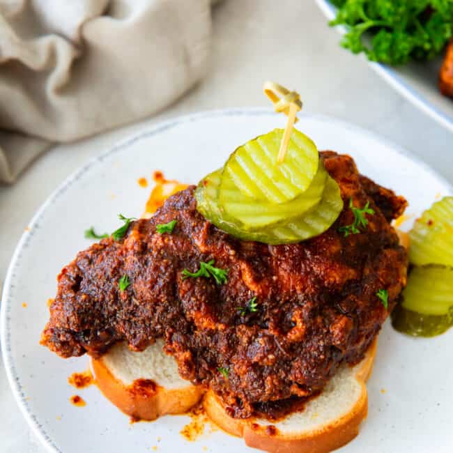piece of nashville hot chicken on a slice of white bread topped with pickles