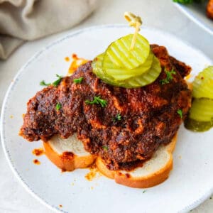 a piece of nashville hot chicken on a slice of bread topped with pickles.