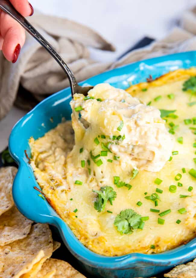 hand using a spoon to scoop white chicken enchilada dip out of a blue baking dish