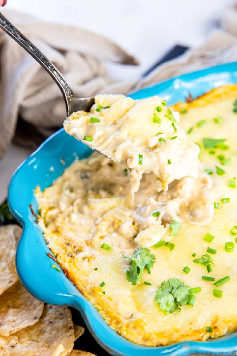 spoon scooping white chicken enchilada dip out of a blue baking dish