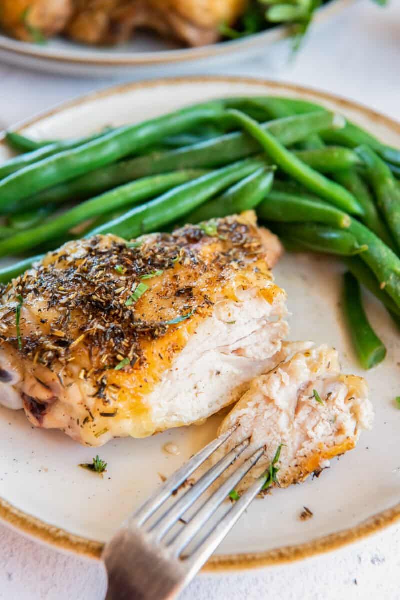 baked chicken thigh on a white plate with green beans and a fork