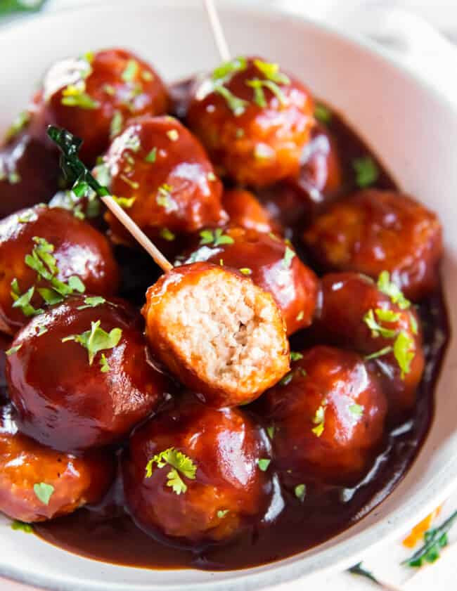 bbq chicken meatballs in a white serving bowl with a bite taken from one meatball