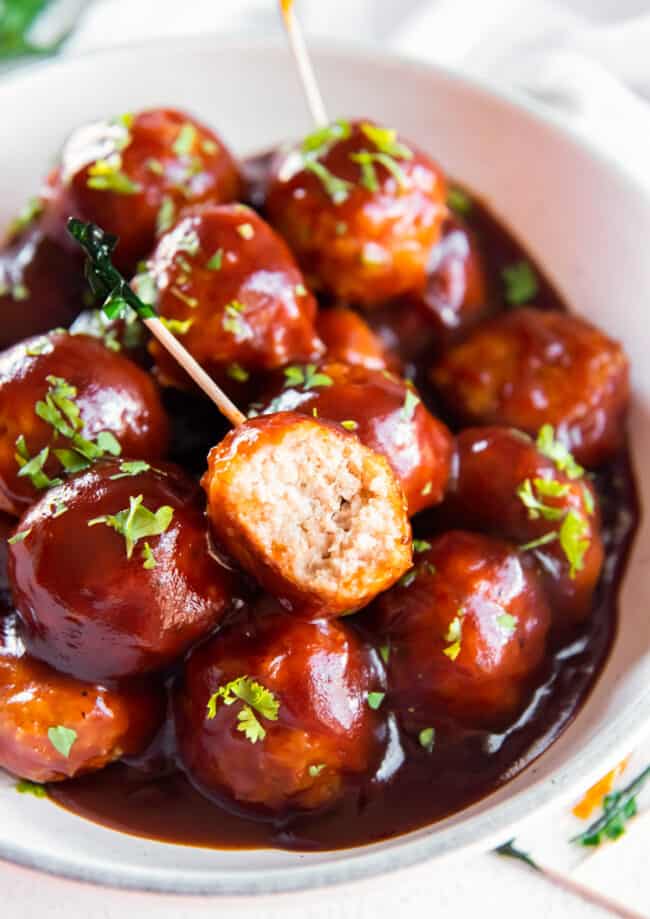 bbq chicken meatballs in a white serving bowl with a bite taken from one meatball