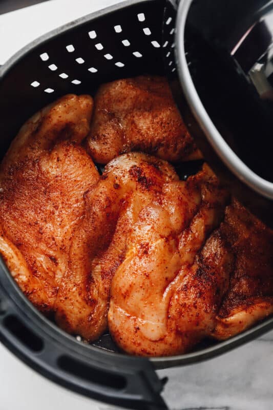 seasoned chicken breasts in an air fryer basket before cooking