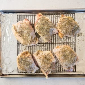 seasoned chicken thighs on a rack on a baking sheet before baking