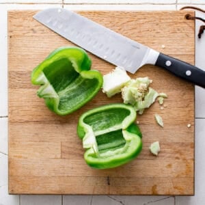 green bell pepper cut in half on a wood cutting board
