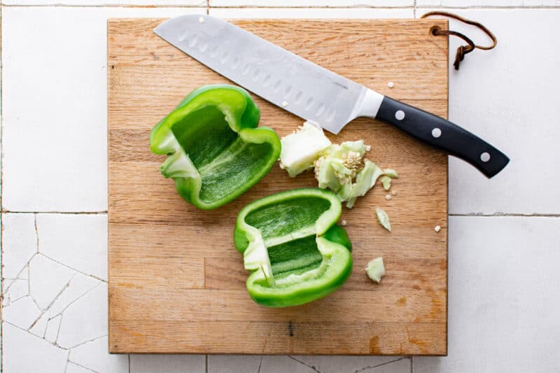 green bell pepper cut in half on a wood cutting board
