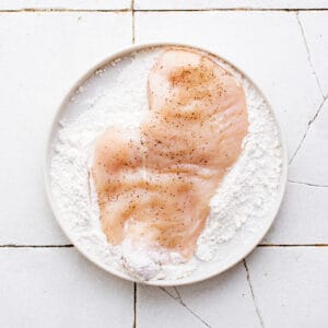 flour on a plate with a chicken breast on top