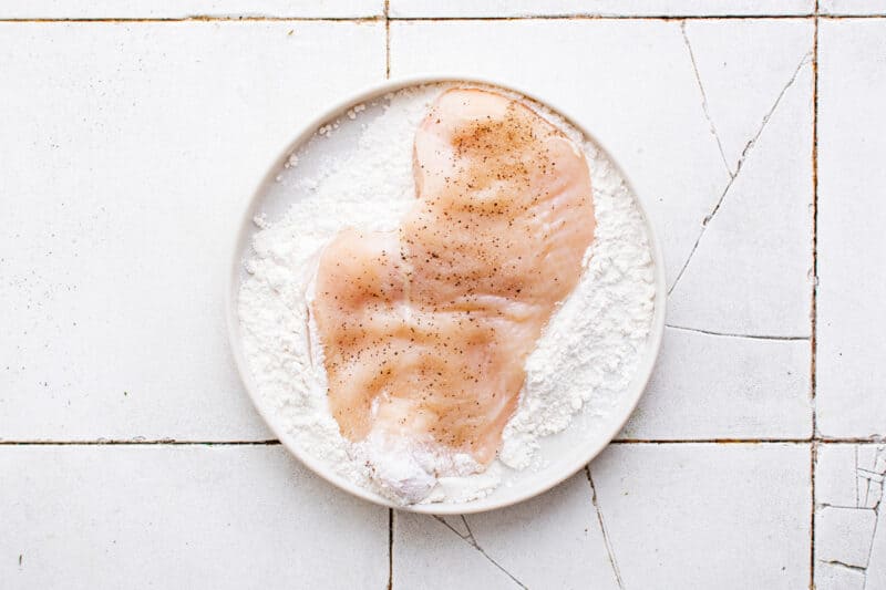 flour on a plate with a chicken breast on top