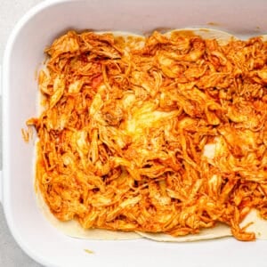 shredded chicken on top of tortillas in a white baking dish