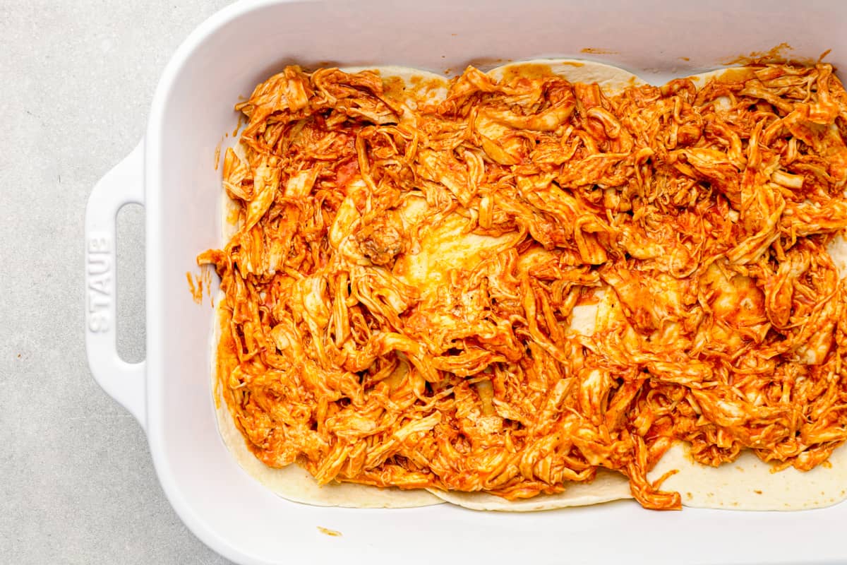 shredded chicken on top of tortillas in a white baking dish