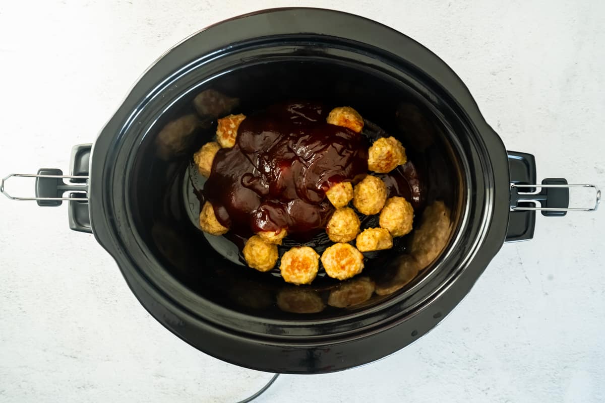 bbq sauce on top of chicken meatballs in a crockpot
