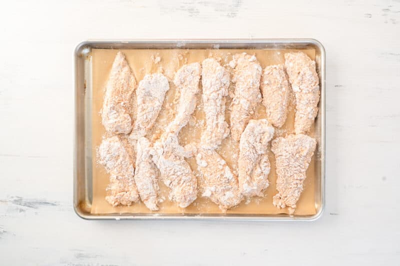 breaded chicken tenders on a parchment paper lined baking sheet