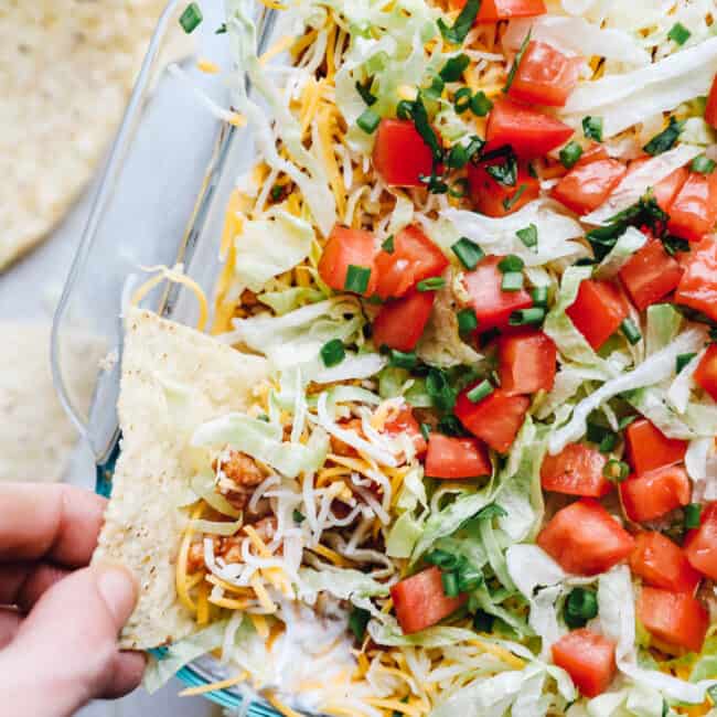 hand dipping a chip into layered chicken taco dip