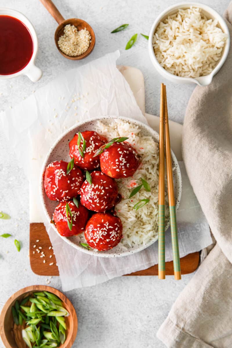overhead image of sweet and sour chicken meatballs with rice on a white plate with chopsticks