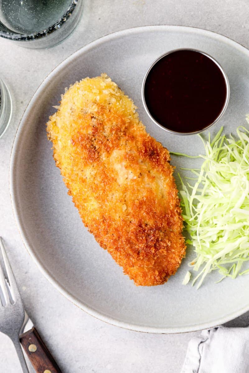 overhead view of chicken katsu with tonkatsu sauce and shredded cabbage on a white plate.