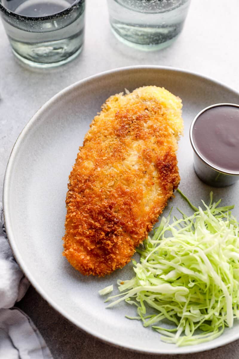 chicken katsu with tonkatsu sauce and shredded cabbage on a white plate.
