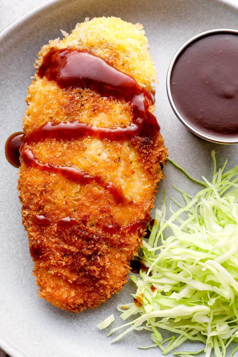 chicken katsu with tonkatsu sauce and shredded cabbage on a white plate.
