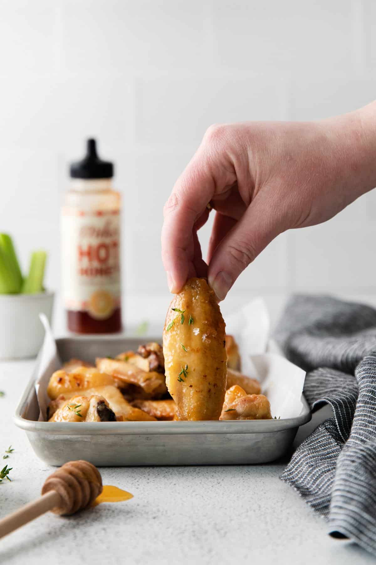 hand grabbing a hot honey chicken wing from a baking sheet.