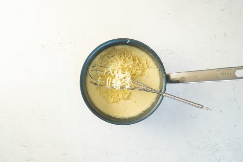 cheeses added to mac and cheese sauce in a saucepan with a whisk.