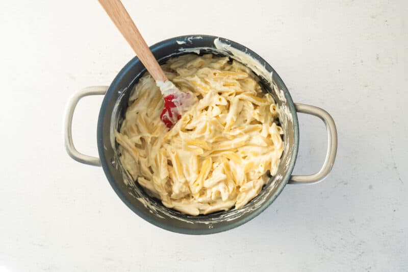 sauced mac and cheese in a pasta pot with a rubber spatula.