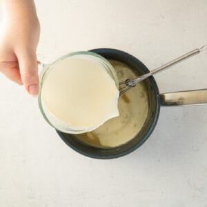 cream added to mac and cheese sauce in a saucepan with a whisk.