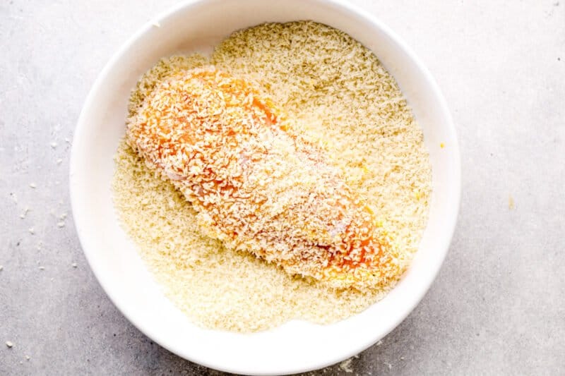 chicken breast dipped in panko breadcrumbs in a white bowl.