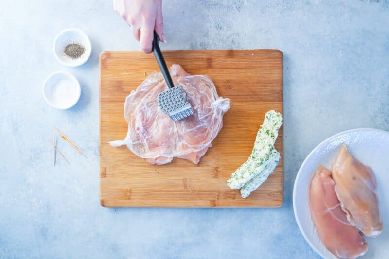 overhead view of chicken breast being pounded thin on a wood cutting board.