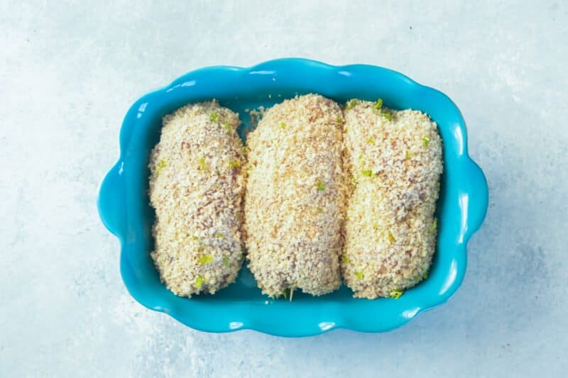 overhead view of 3 unbaked chicken kievs in a blue baking dish.