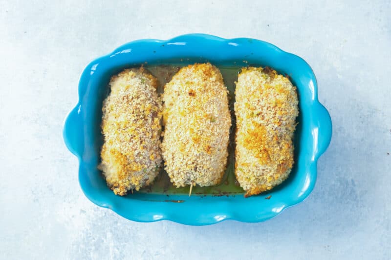 overhead view of 3 baked chicken kievs in a blue baking dish.