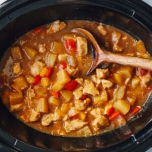 cooked crockpot hawaiian chicken in a crockpot with a wooden spoon.