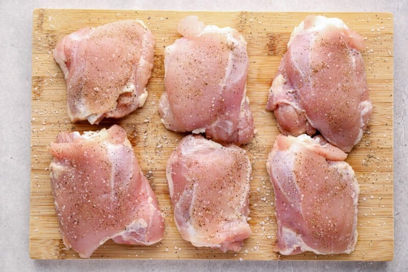6 raw chicken thighs on a wood cutting board.