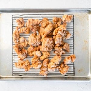 general tsos chicken pieces after frying on a wire rack set in a baking sheet.